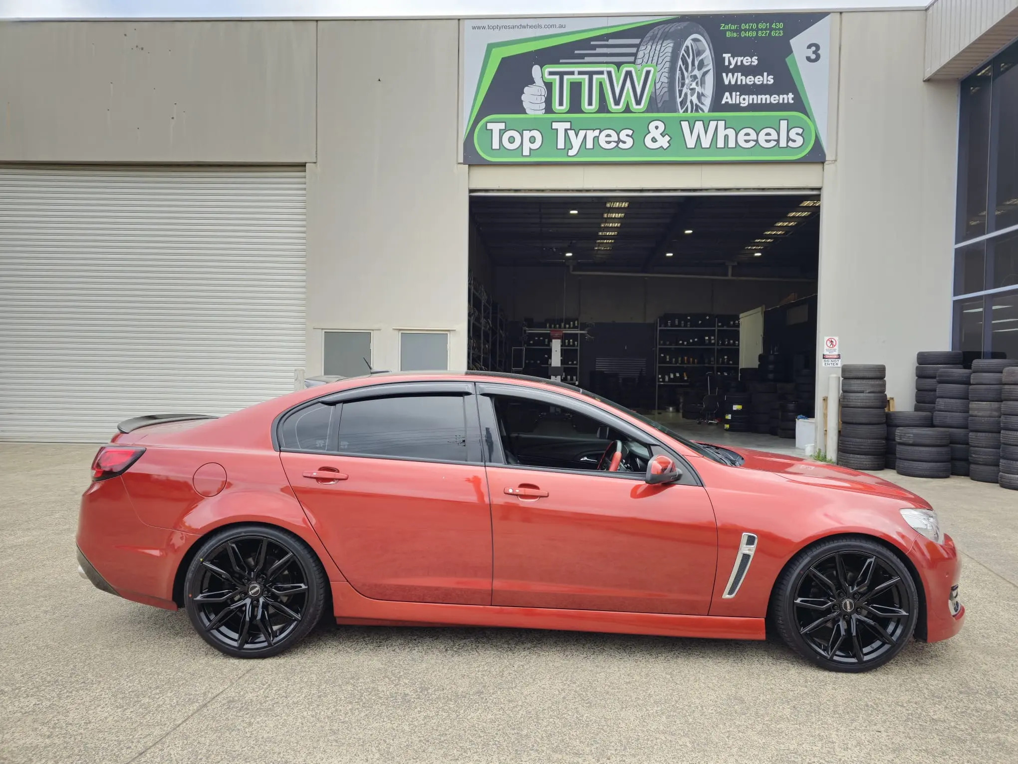 Red sedan with new black alloy wheels outside the workshop